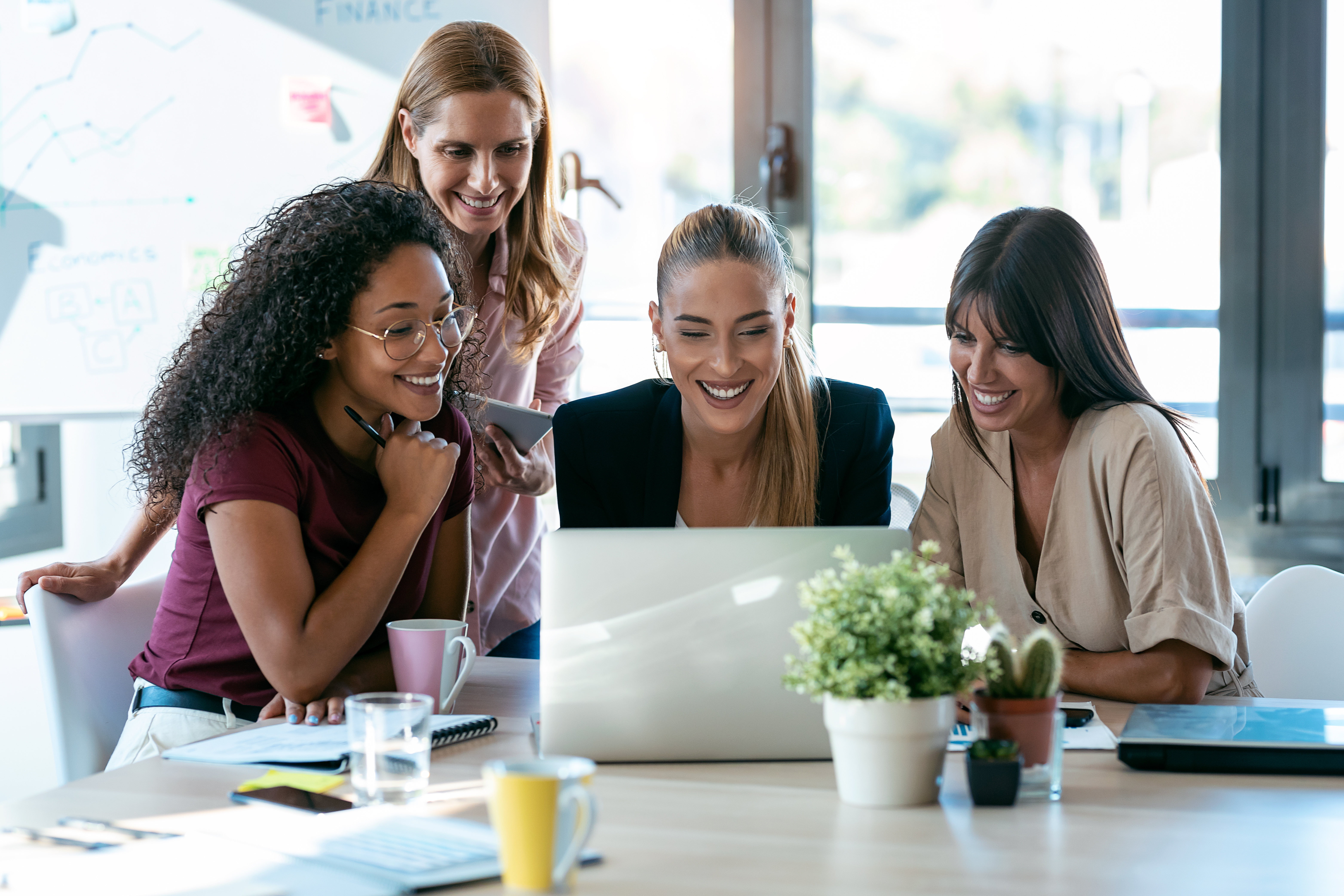 Group of four women gathered around a laptop