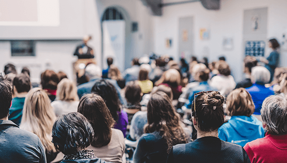 A large room of people listening to someone speak at a conference